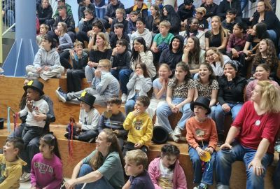 Zu sehen sind die Besucher des Schulfestes, die auf Stufen des Foyers sitzen.
