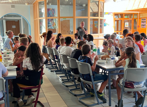 Die Schulgemeinschaft sitzt an großen Tischen und wartet auf das Essen.