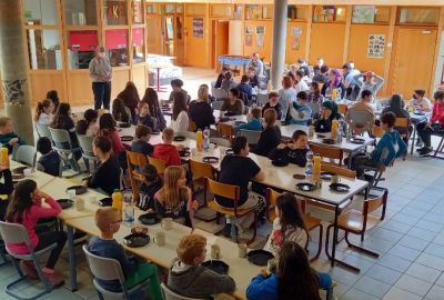Zu sehen ist die Schulgemeinschaft im Foyer an langen Tischen