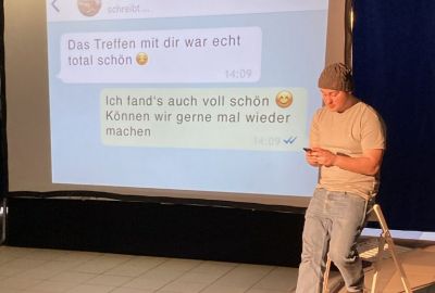 Ein Schauspieler lehnt an einem Stuhl und schreibt eine Nachricht.