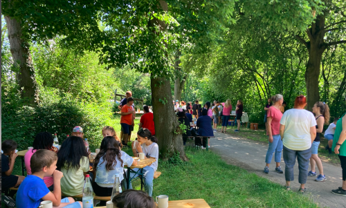 Menschen stehen im Garten. andere sitzen an den Tischen und essen Würstchen.