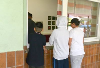 Zu sehen sind drei Schüler die vor dem Pausenverkaufsraum stehen