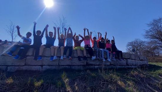 Kinder in Sportkleidung jubeln auf einer Steinmauer