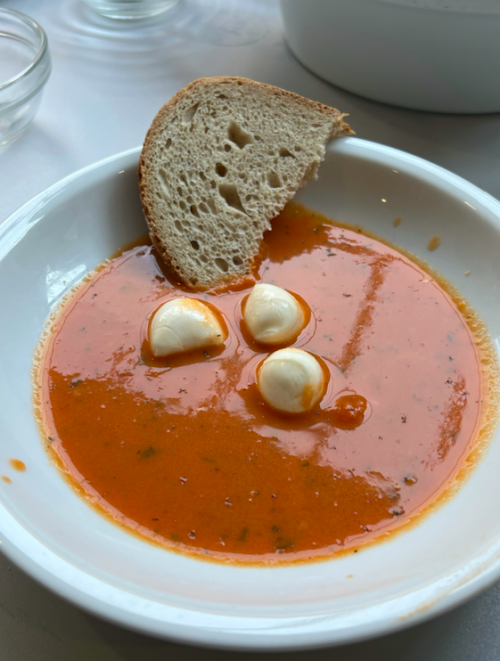 Ein angerichteter Teller mit Tomatensuppe, Mozzarella-Bällchen und Brot ist zu sehen.
