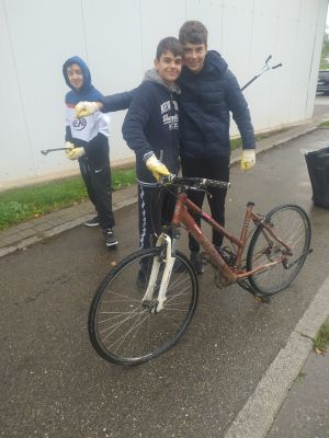 Zu sehen sind Kinder beim Müll sammeln. Sie haben ein Fahrrad gefunden.