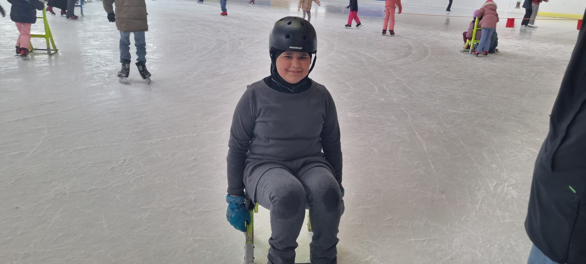 Ein Mädchen sitzt mit einem Fahrradhelm auf einer Eislaufhilfe